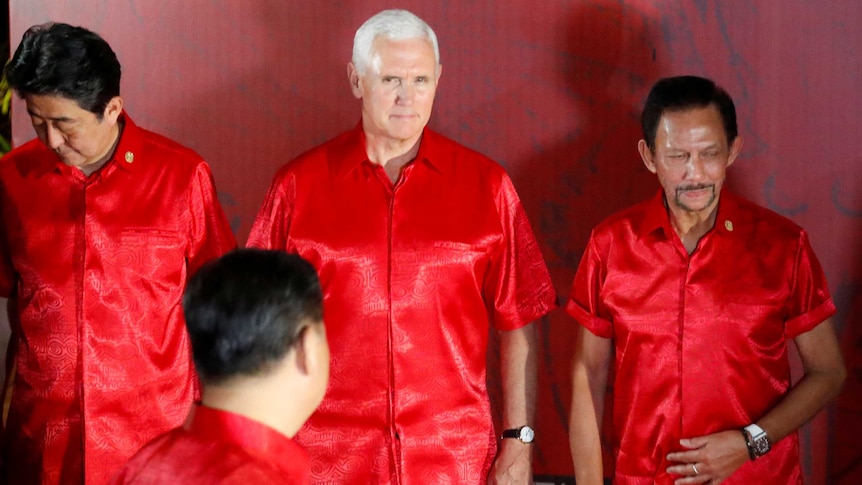 Mike Pence looks at Xi Jinping, whose face is obscured. Everyone is wearing matching red shirts.