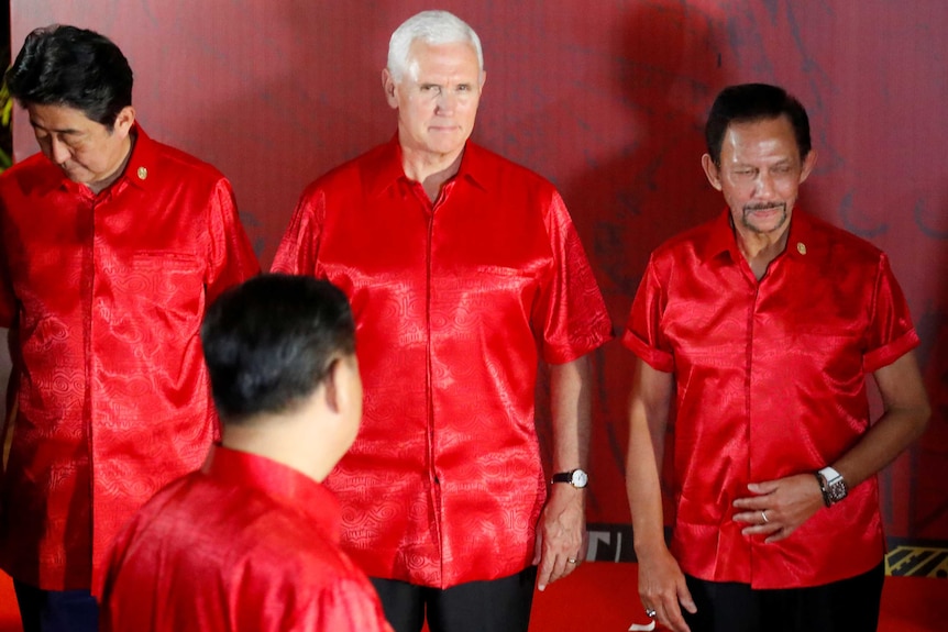 Mike Pence looks at Xi Jinping, whose face is obscured. Everyone is wearing matching red shirts.