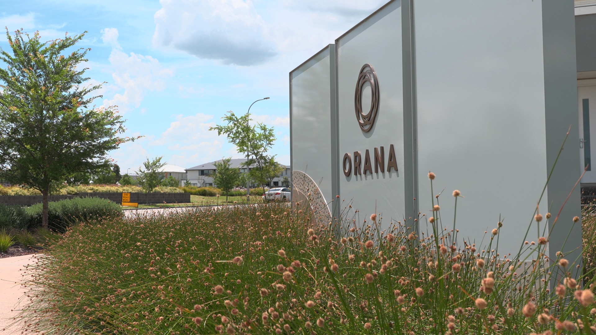 Uma placa na entrada de uma fazenda que diz Orana e plantas na frente dela.