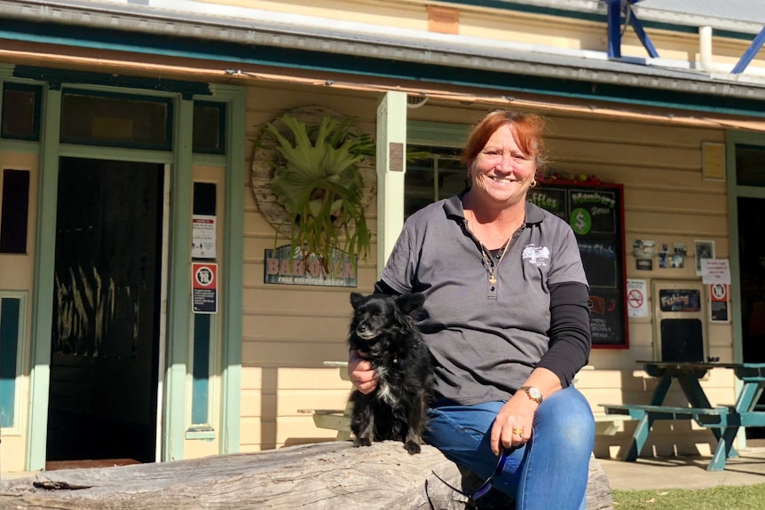 Middle aged woman sitting with a dog in front of a pub.