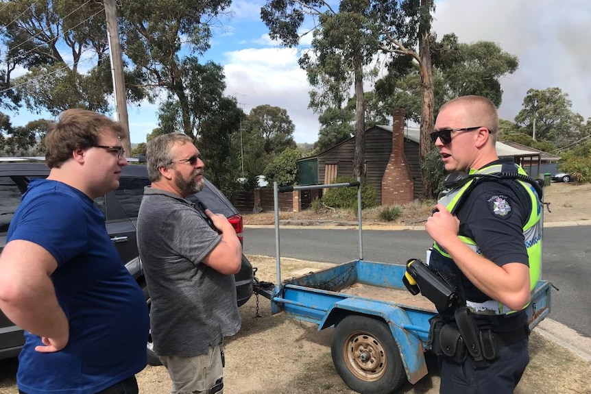 A police officer speaks to residents in a street lined with gum trees.