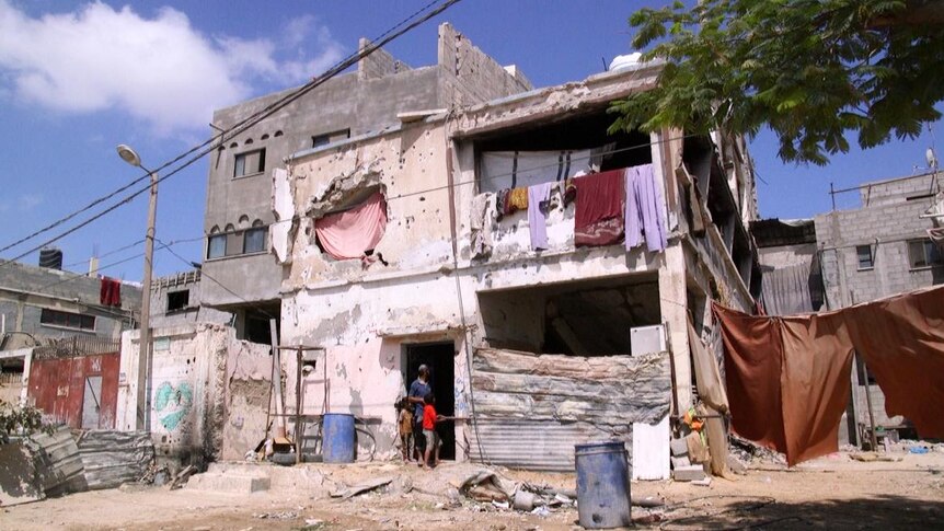 Members of the Mosabeh family stand at the door to their home, which was half destroyed in a missile strike.