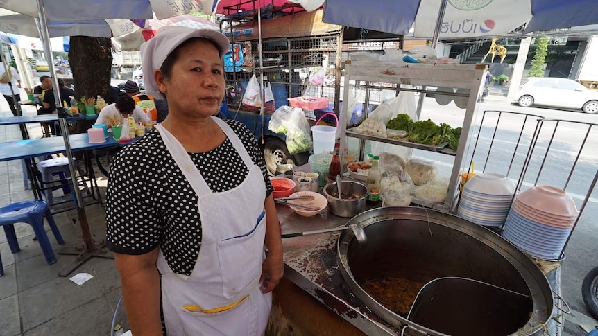Woman stands in front of cooking pot at a sidewalk eatery