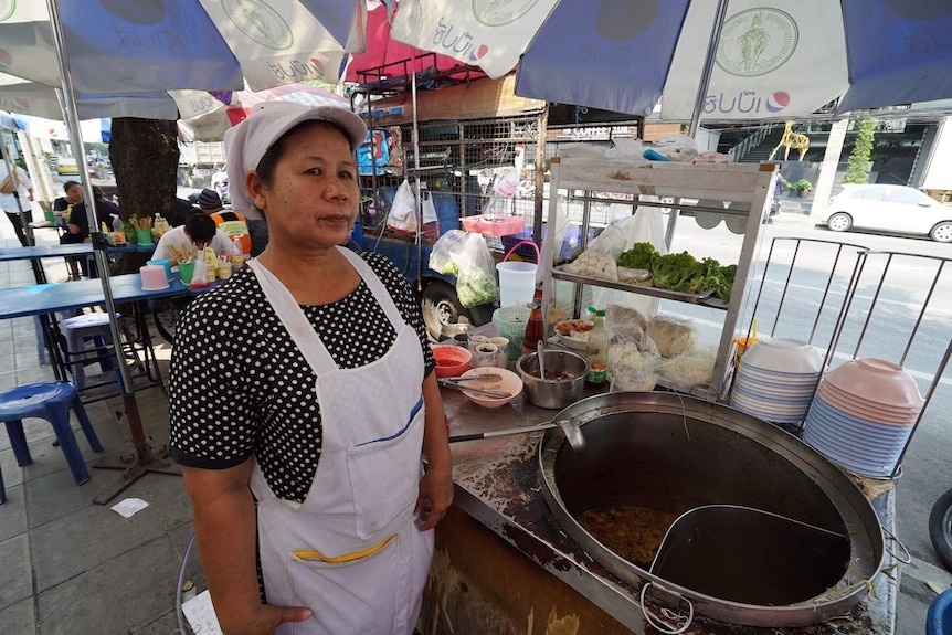 Woman stands in front of cooking pot at a sidewalk eatery