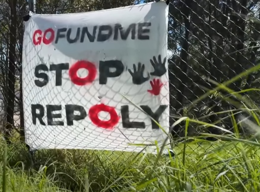 A banner opposing a plastic factory development is stuck to a chain-link fence.
