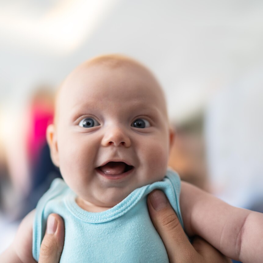 An image of a smiling baby. They're being held up to face the camera.