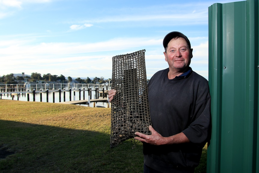 A man holding a net while standing in front of an oyster farm.