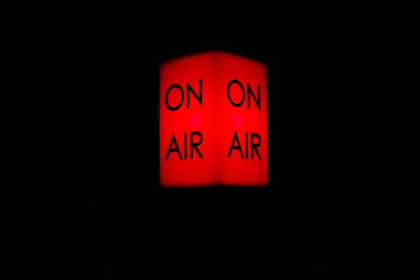 A red rectangular light that says 'on air' illuminated in a pitch black room.