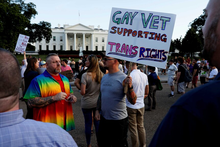 At a protest outside the White House, a man holds a sign that reads 'Gay vet supporting trans rights'.