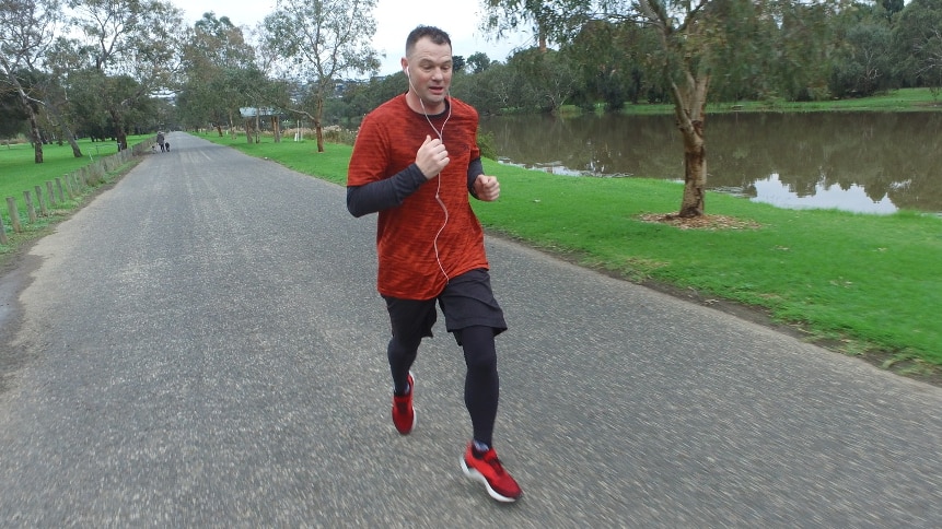 A man in red and black running clothes jogs along a path in a park