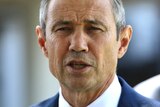 A tight head and shoulders shot of WA Health Minister Roger Cook wearing a suit and tie and talking during a media conference.