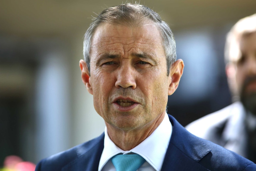 A tight head and shoulders shot of WA Health Minister Roger Cook wearing a suit and tie and talking during a media conference.