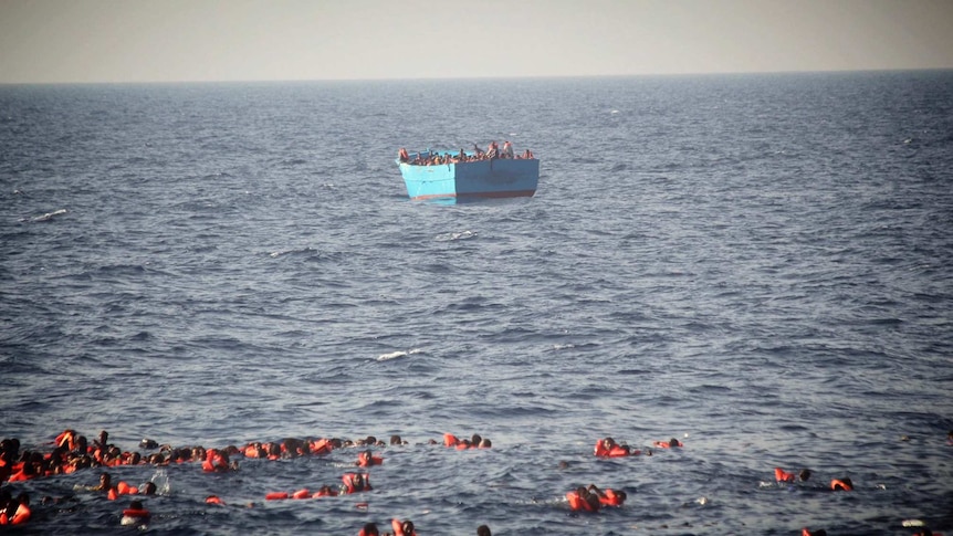 Asylum seekers wearing life vests are seen floating in the water before being rescued at sea.