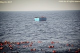 Asylum seekers wearing life vests are seen floating in the water before being rescued at sea.