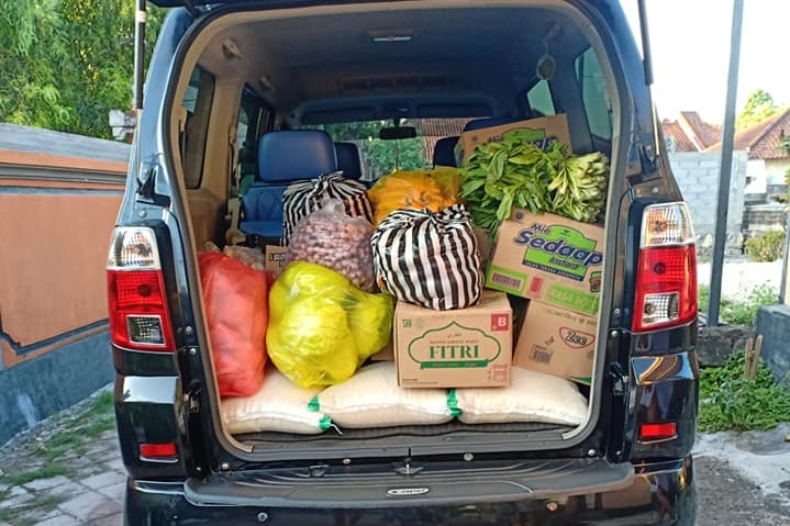 A car boot full of food like rice and vegetable, with trays of eggs on the ground.