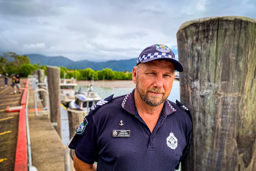 A man in a police uniform leans against a pylon at the end of a wooden jetty.