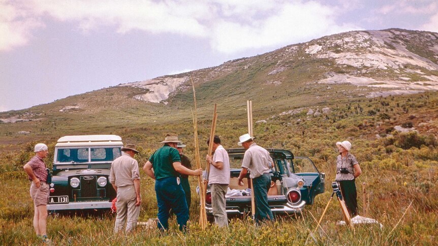 A team of researches in khakis at work in a scrub-dotted landscape at the bottom of a mountain.