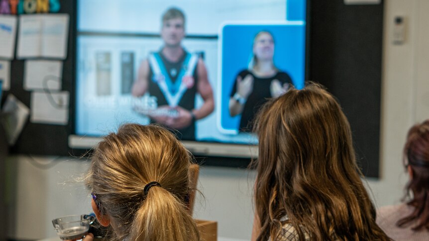 Two girls look at a projection of Port Adelaide player Ollie Wines talking about healthy eating