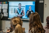 Two girls look at a projection of Port Adelaide player Ollie Wines talking about healthy eating