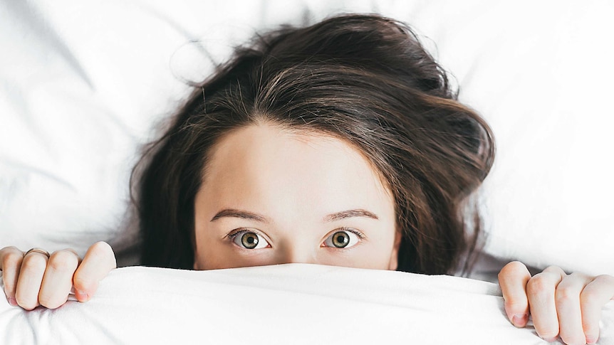 A woman poking the top of her head out from under the blankets in bed.