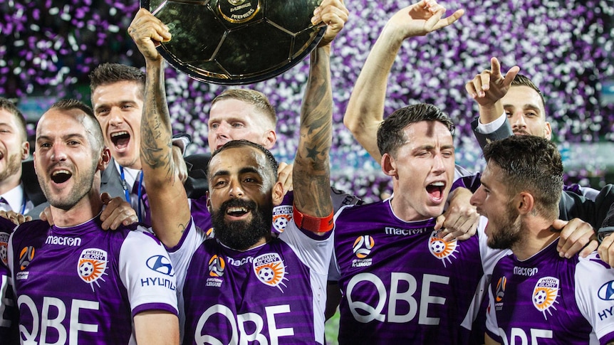 Diego Castor holds the A-League Premiers Plate trophy above his head with his Perth Glory teammates behind him