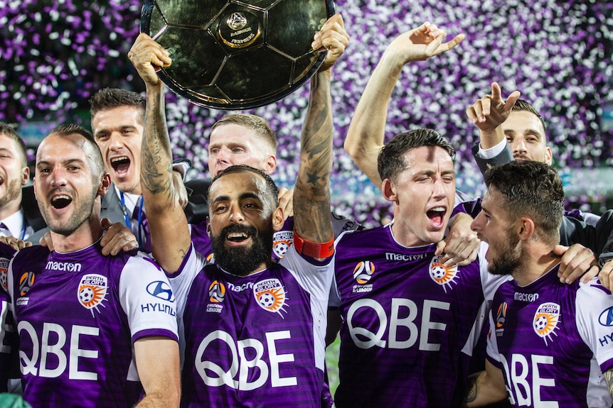 Diego Castor holds the A-League Premiers Plate trophy above his head with his Perth Glory teammates behind him