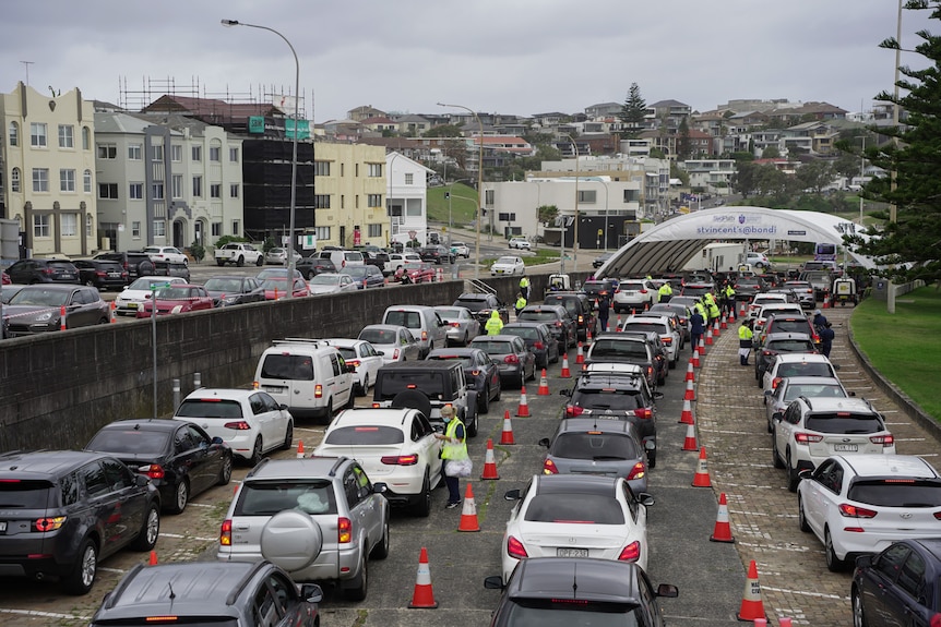 Cars queuing at a drive-through testing clinic on an overcast day with buildings in the background