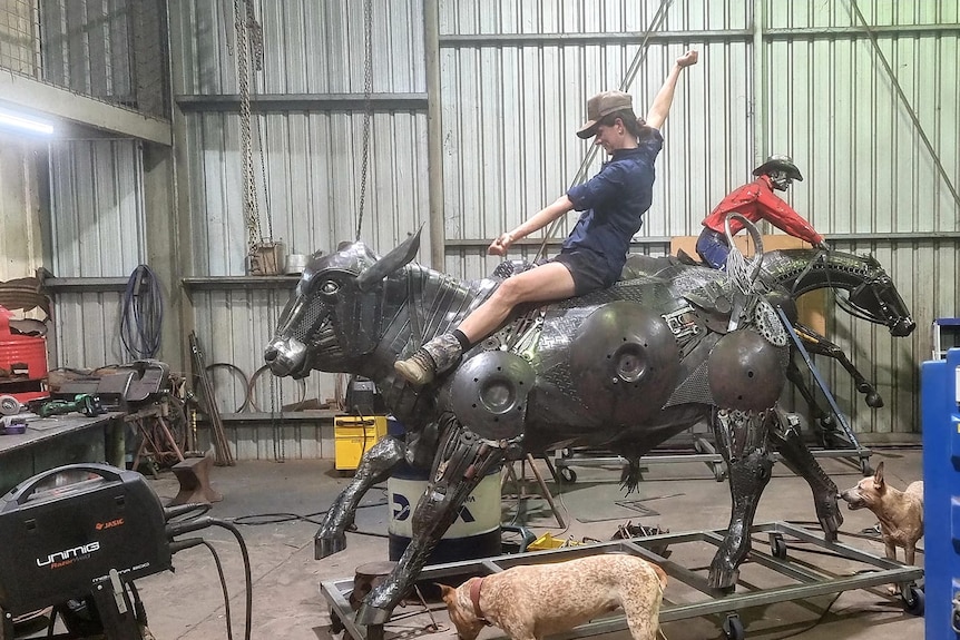 A woman rides a metal sculpture of a bullock