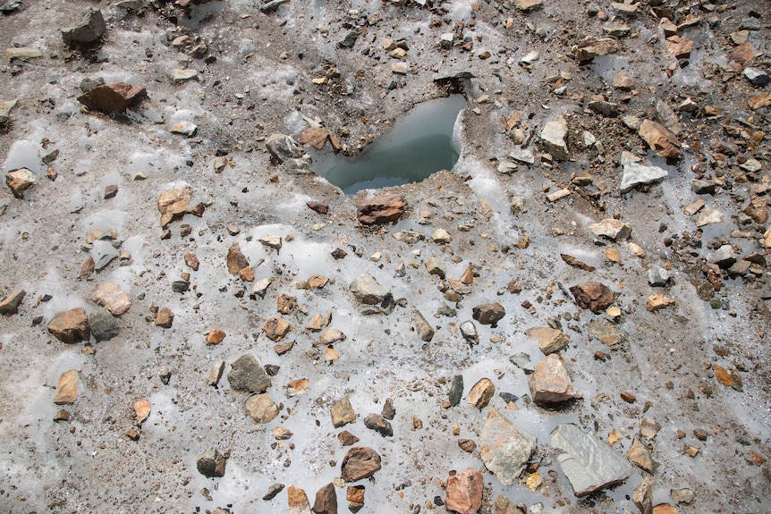 Rocks lay on to op of ice and around a small body of water. 