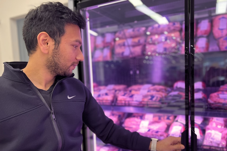 a man opens a fridge door in a supermarket meat aisle