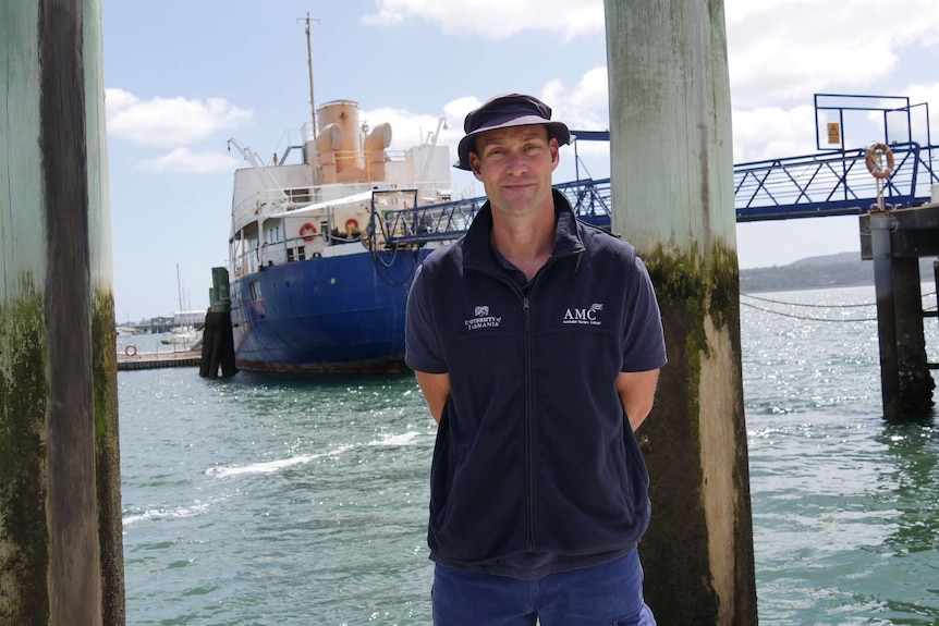 A man stands on a dock in front of a ship.