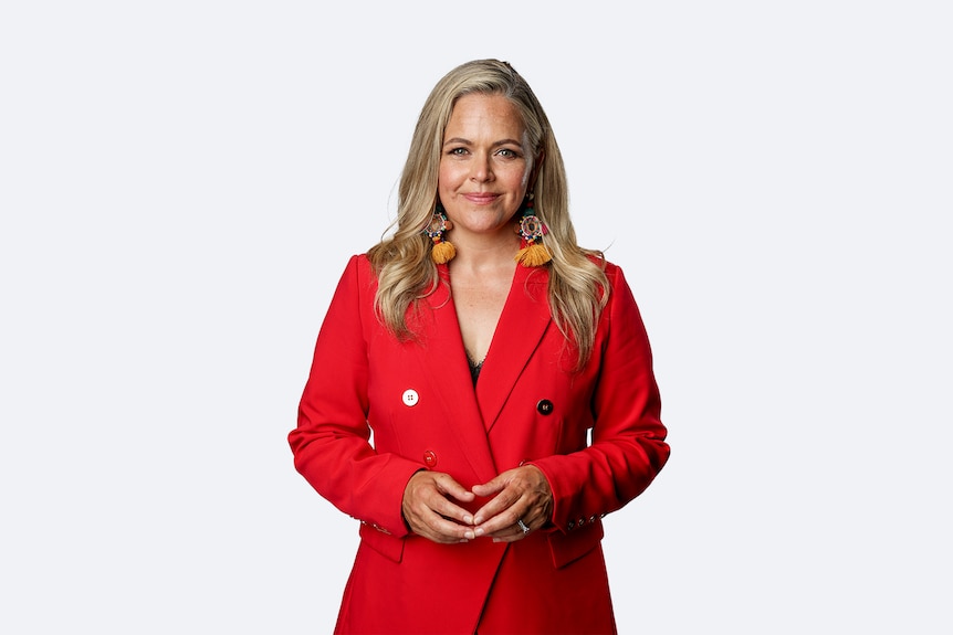 Taryn Brumfitt is a pale-skinned woman, with long blonde hair. She is wearing a bright red blazer.