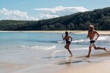 A man and a woman run into the water on a beautiful beach. Good generic