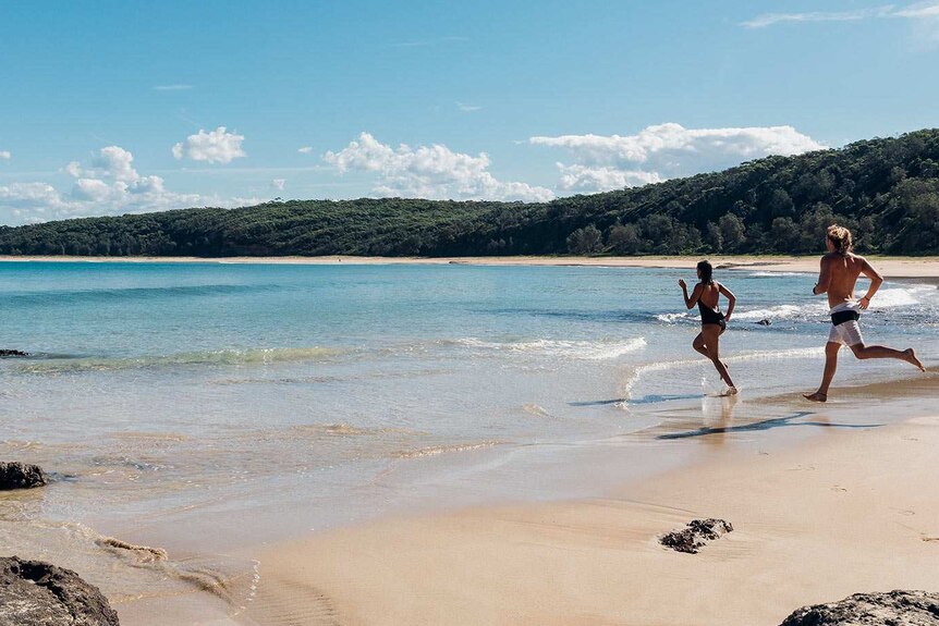 A man and a woman run into the water on a beautiful beach. Good generic