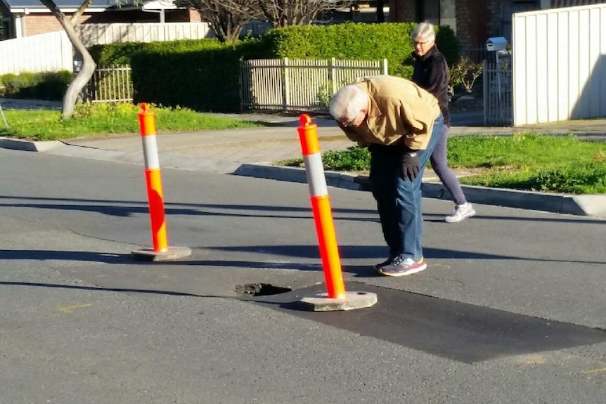 Residents check the depth of a pothole that is believed to have formed due to a leaking sewer.