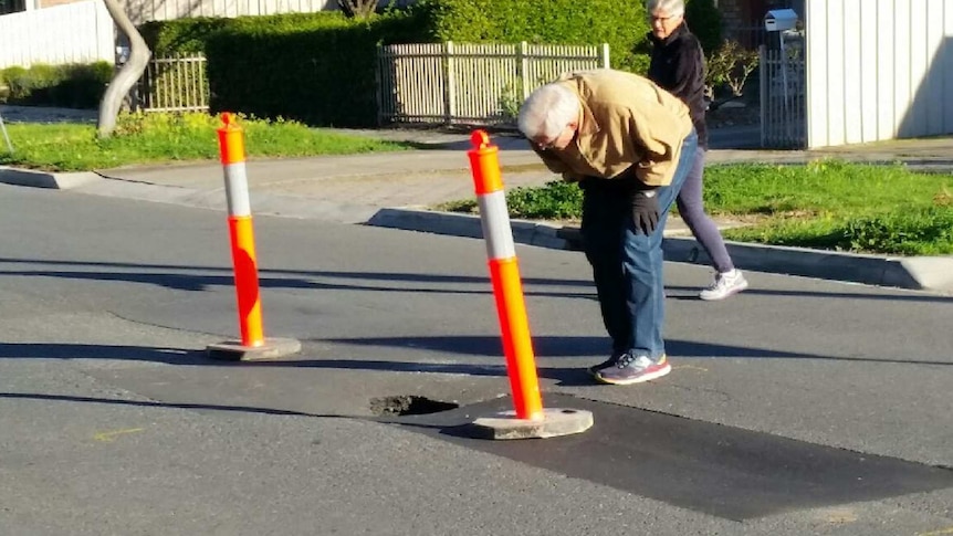 Residents check the depth of a pothole that is believed to have formed due to a leaking sewer.