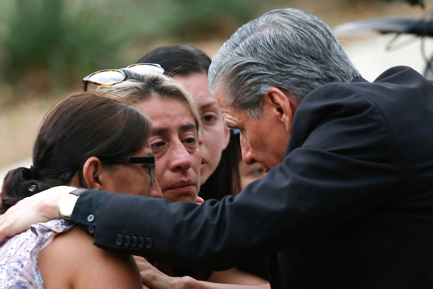 Archbishop of San Antonio Gustavo Garcia-Siller bends down and hugs three women