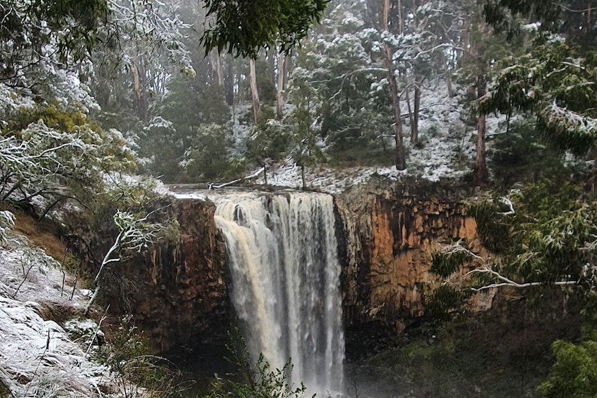Snow falls near a running waterfall.