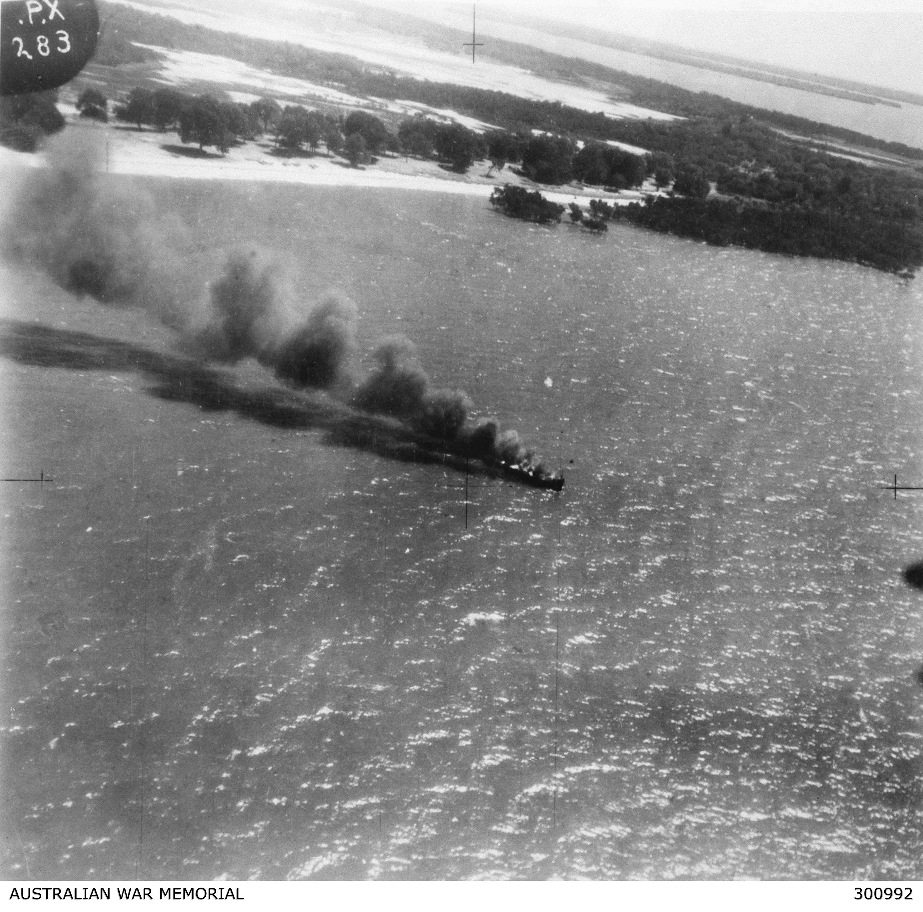 A black and white, historical photo showing a ship on fire in Darwin Harbour.