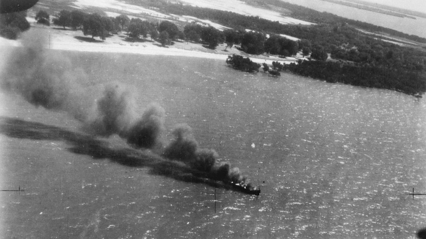A black and white, historical photo showing a ship on fire in Darwin Harbour.