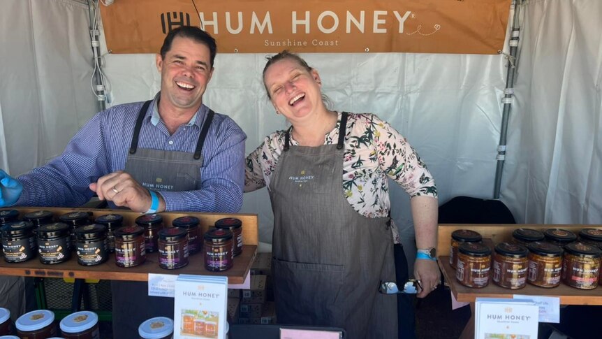 A smiling couple poses behind jars of honey.