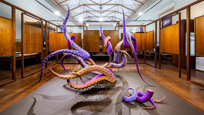 Purple coloured textile sculpture made from detached tentacles, in gallery space surrounded by wooden panels.