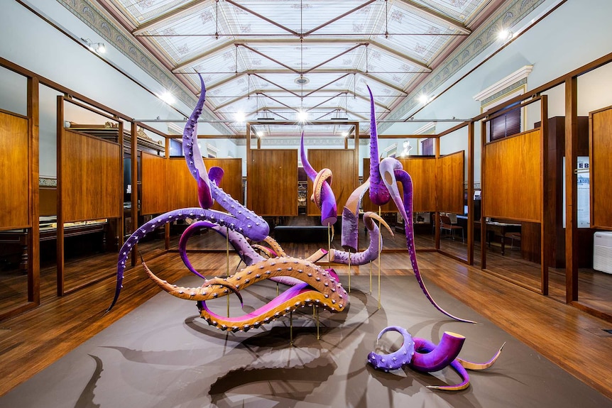 Purple coloured textile sculpture made from detached tentacles, in gallery space surrounded by wooden panels.