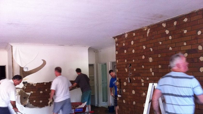 People rip off wall sheeting inside flood-damaged house on Brisbane River at Chelmer