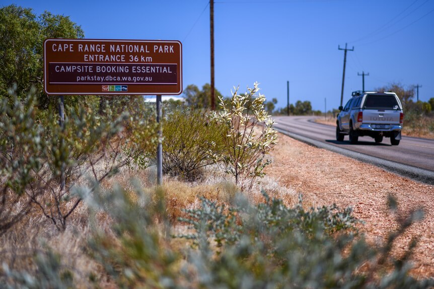A car drives past a sign marking the entrance to the Cape Range National Park.