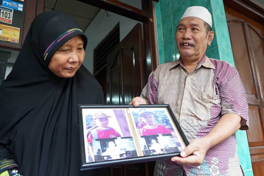 Setijoko and his wife hold framed photographs of Riky and Riko Prawoto, two twins from Indonesia's 'twin village'.