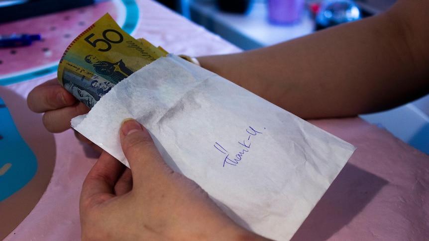 Hands holding a cash-filled envelope with "thank U" written on it.
