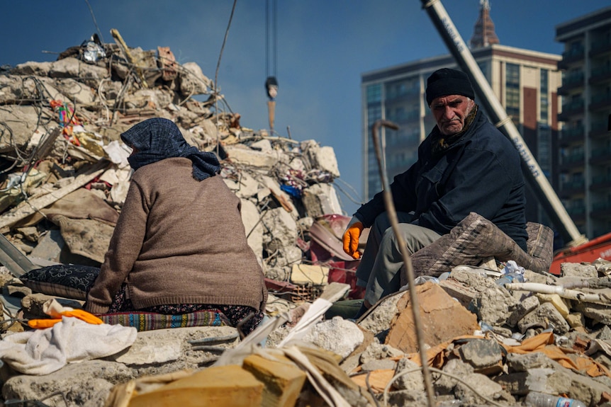 An old man and a woman sit on rubble.