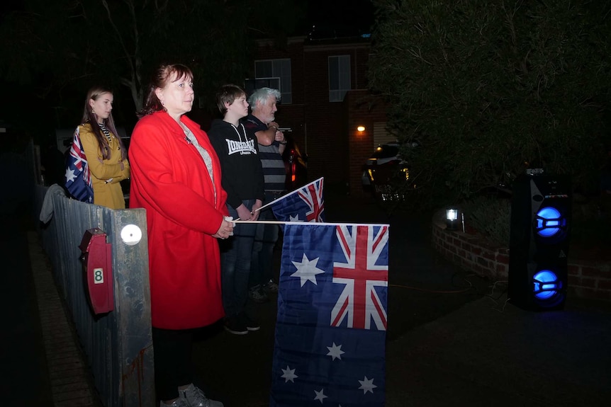 A family stands together outside, holding Australian flags