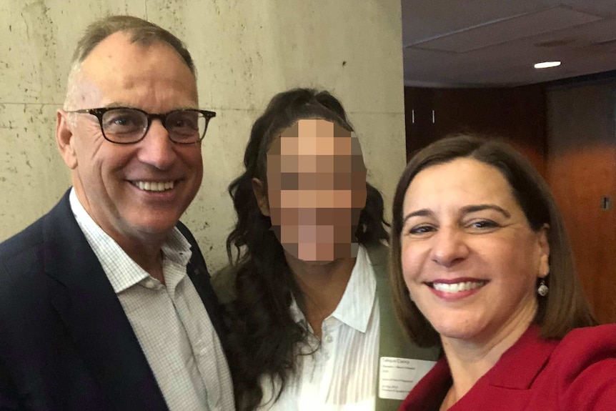 Man in woman and glasses stands smiling next to two women, one with face pixelated